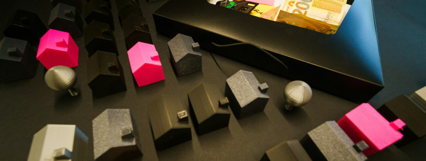 Miniature houses arranged with cash in an open box.