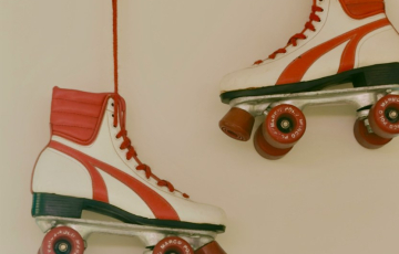Two white and red roller skates hanging by red laces against a plain wall