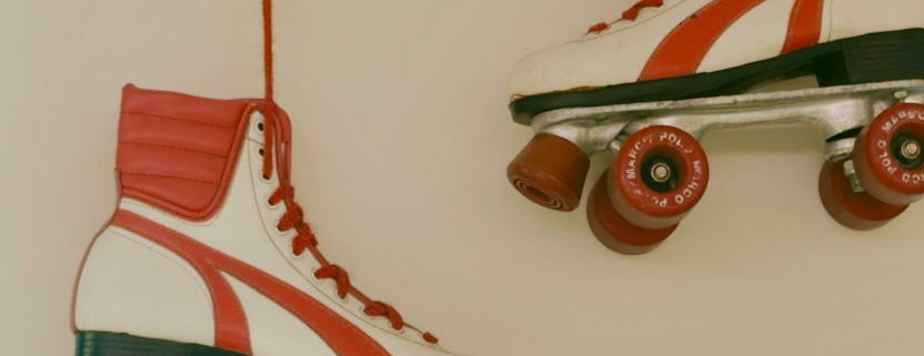 Two white and red roller skates hanging by red laces against a plain wall