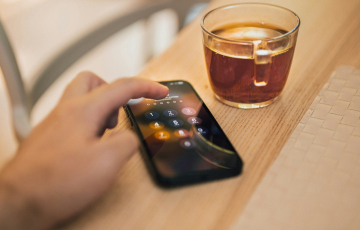A person holding a cell phone next to a cup of coffee